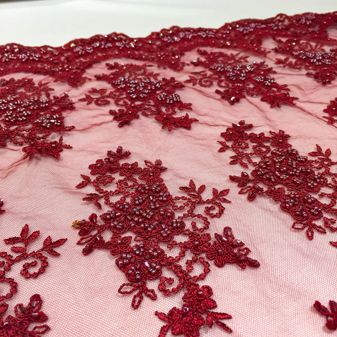 Stoff von rotem, besticktem Tüll mit floralen Motiven und glitzernden Verzierungen auf einem rosa Hintergrund.