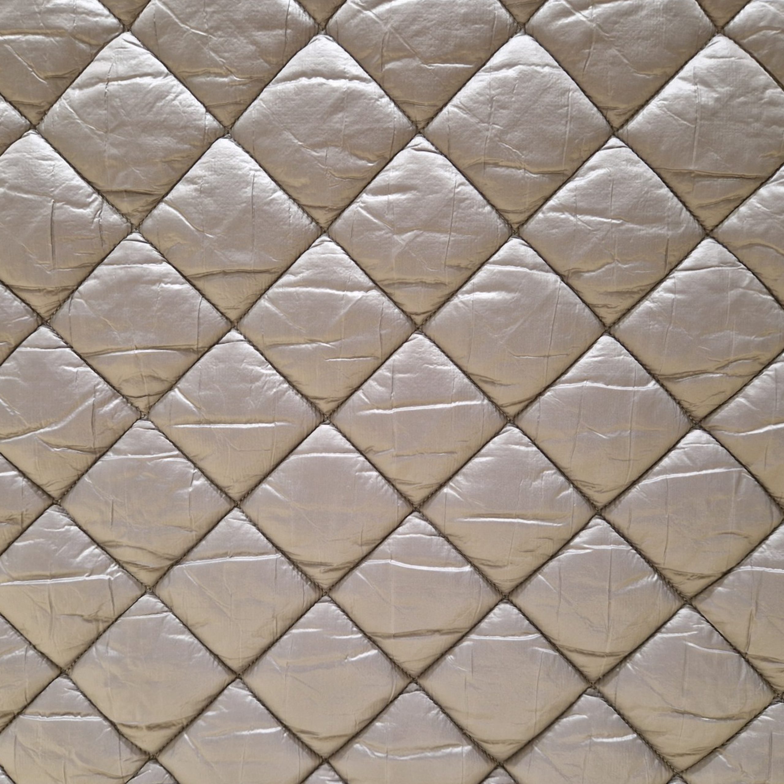 Stoff von einem gesteppten, quadratischen Muster in sanften Beigetönen mit glänzender Oberfläche.