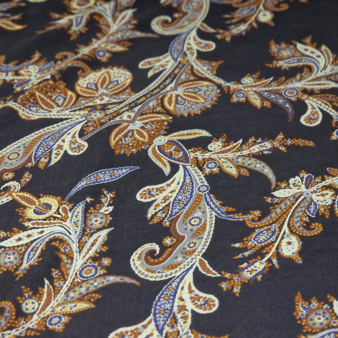 Stoff von eleganten Paisleymustern in Blau, Braun und Creme auf einem dunklen Hintergrund.