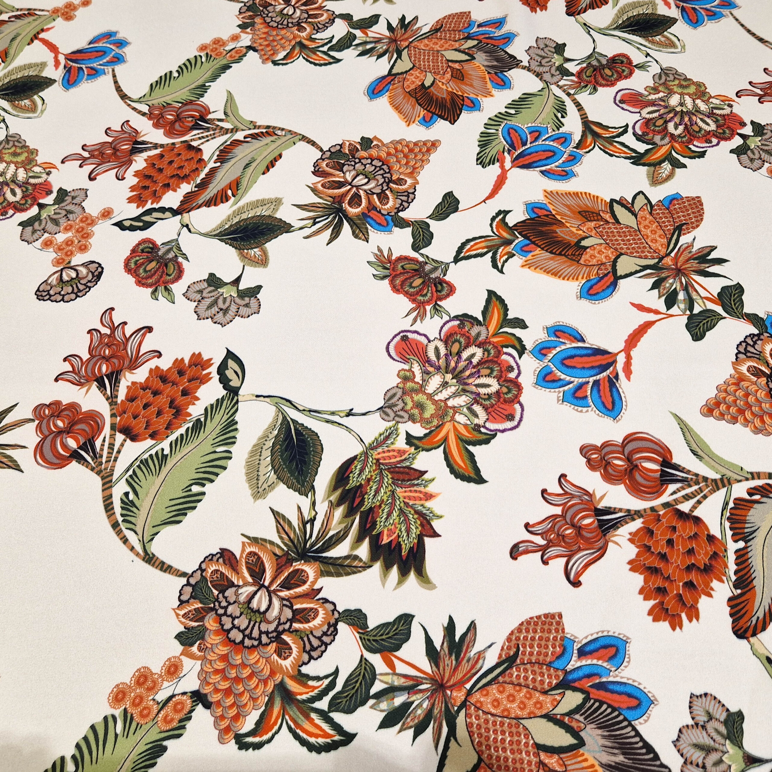 Stoff von bunten Blumen und Blättern auf hellem Hintergrund, mit detaillierten Mustern in Rot, Blau und Grün.