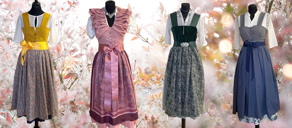 Stoff von vier traditionellen Trachtenkleidern in verschiedenen Farben und Designs, präsentiert auf Schaufensterpuppen.