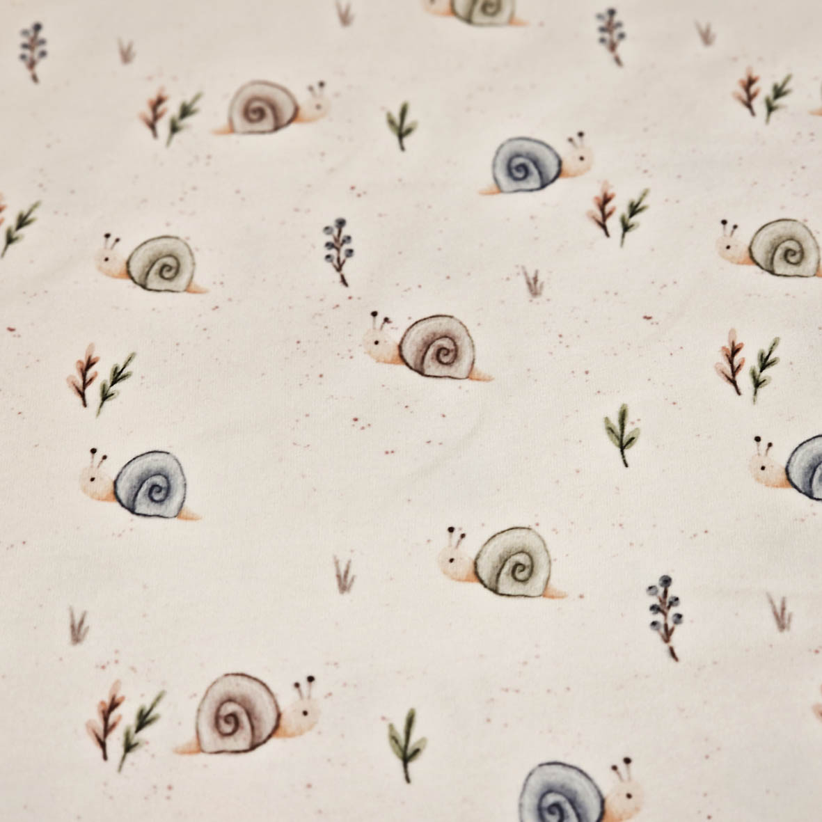 Stoff von Schneckenmuster mit sanften Farben und kleinen Pflanzenmotiven auf hellem Hintergrund.