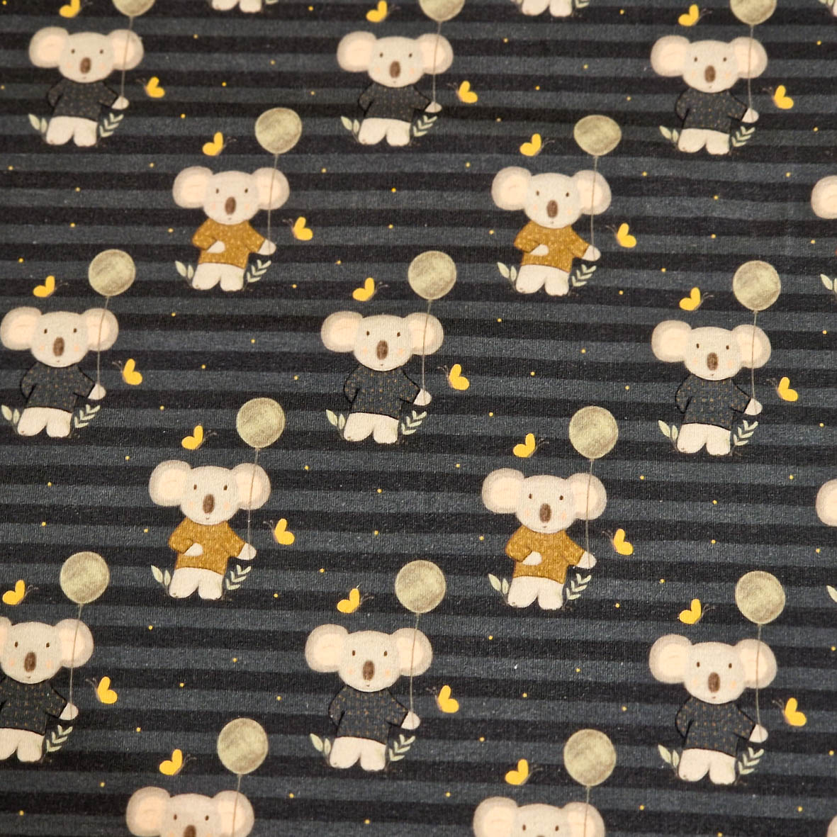Stoff von Koalas in braunen Shirts auf gestreiftem, dunklem Hintergrund mit gelben Bananen und grauen Kreisen.