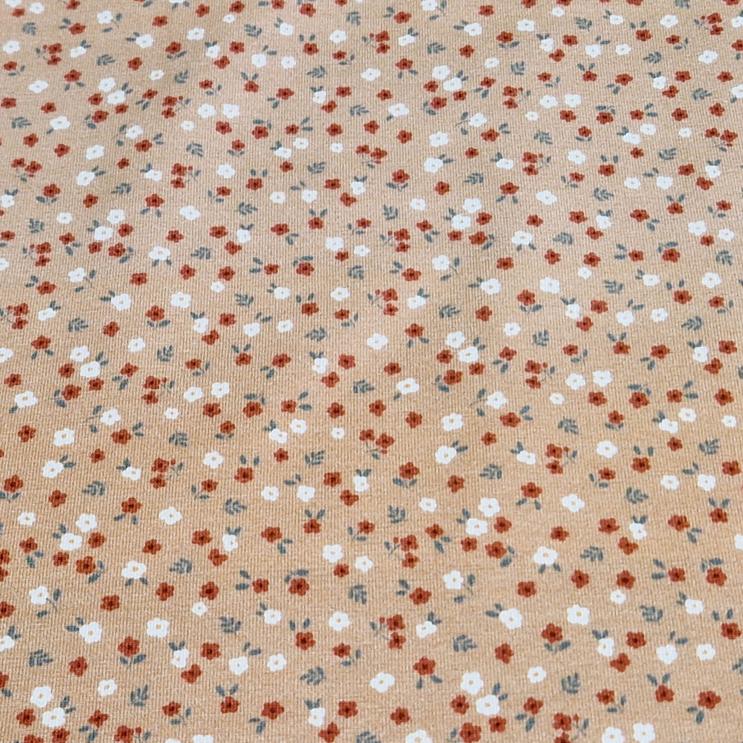 Stoff von einem beigen Hintergrund mit kleinen roten und weißen Blumen sowie grünen Blättern.